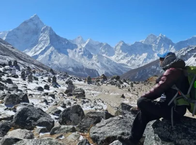 Trekker standing on a mountain trail, viewing Mount Everest in the distance under clear skies