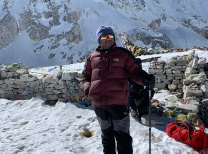 Experienced Nepalese guide standing on a rugged Manaslu Circuit trail with trekking poles, helping trekkers navigate the challenging high-altitude terrain.