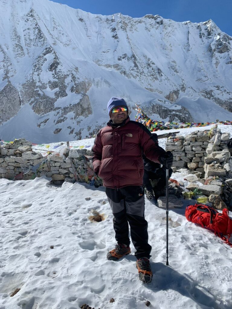 Experienced Nepalese guide standing on a rugged Manaslu Circuit trail with trekking poles, helping trekkers navigate the challenging high-altitude terrain.