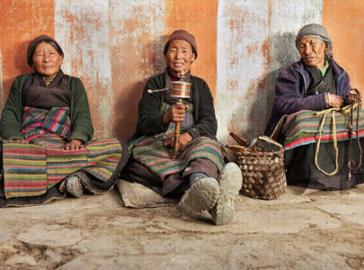 Sherpa elderly woman praying and spinning prayer wheel in Himalayan village